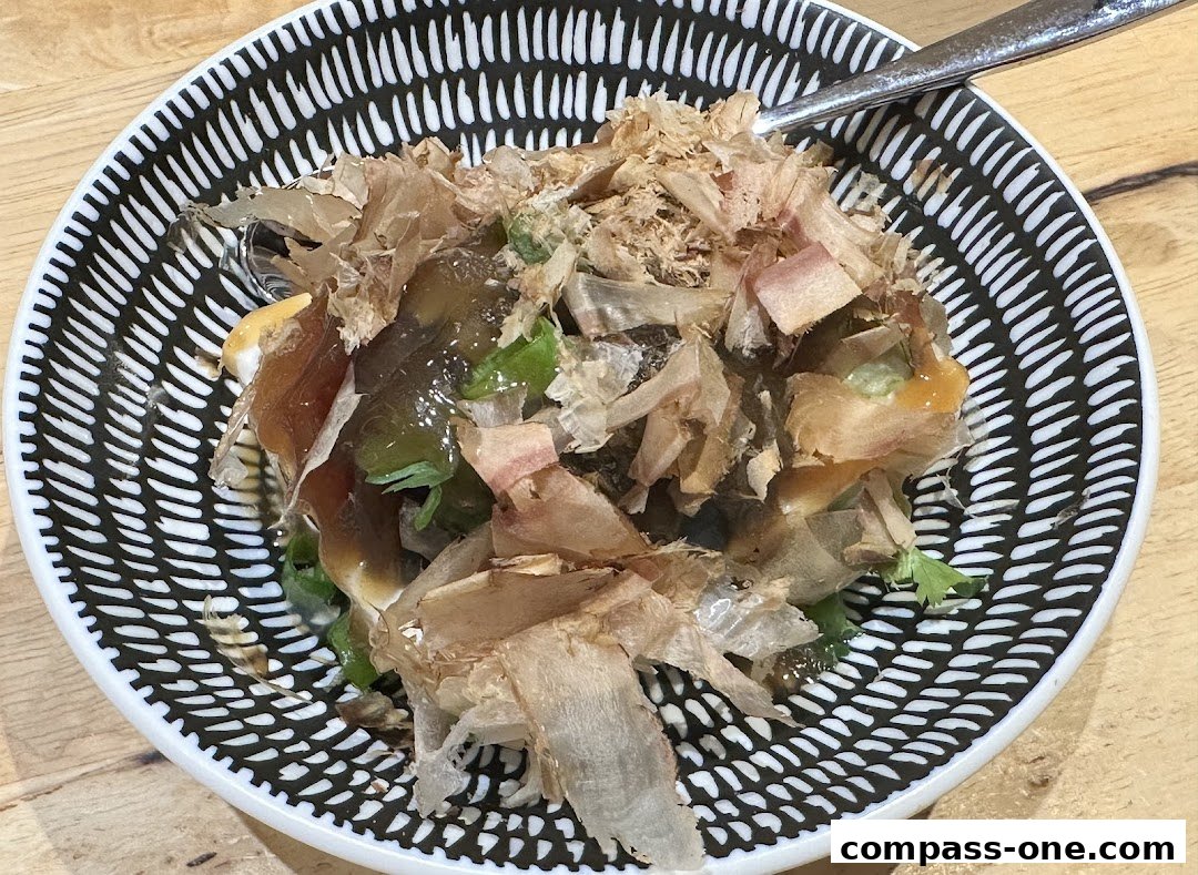 A close-up of a bowl of noodles topped with bonito flakes and other ingredients.