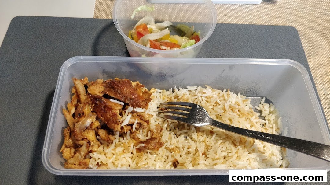 A take-out container filled with seasoned rice and grilled meat, served with a side salad.