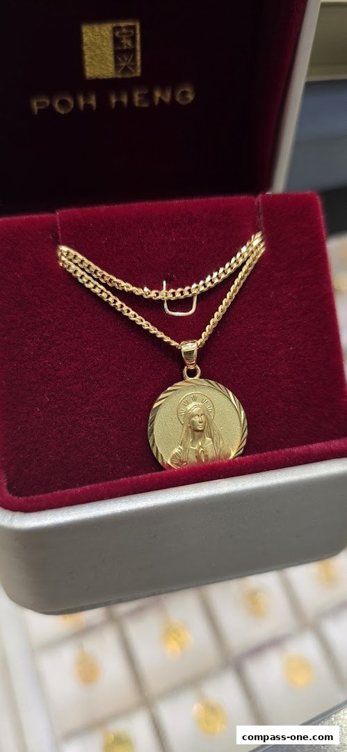 A gold pendant necklace with a religious motif displayed in a velvet jewelry box.