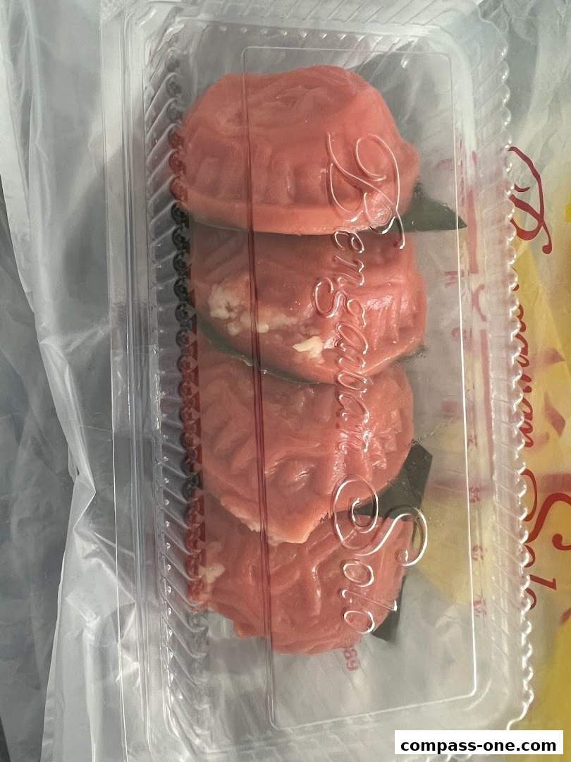 A clear plastic container holding four pink, intricately molded pastries with visible filling.