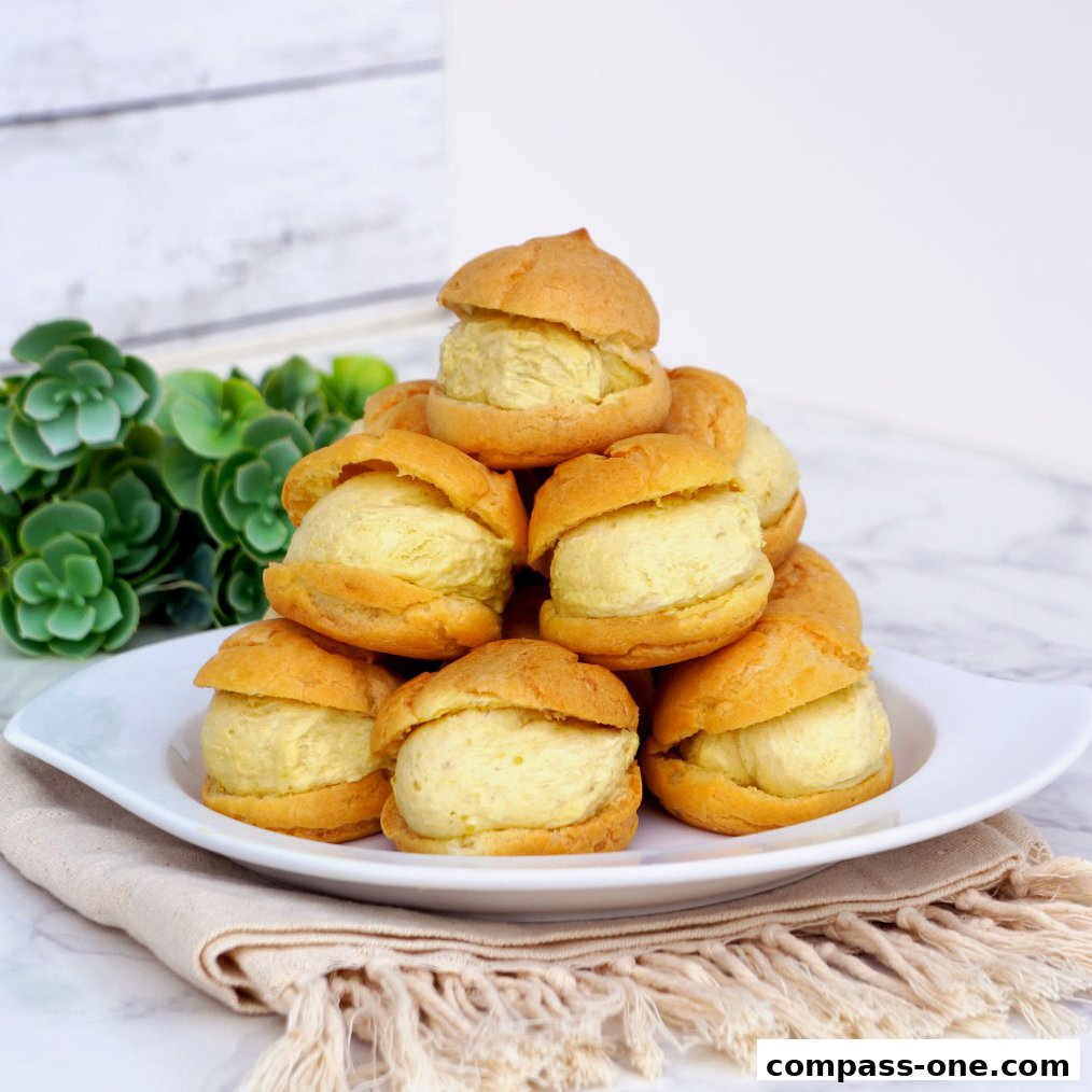 A pile of cream puffs filled with light yellow cream on a white plate with a napkin.