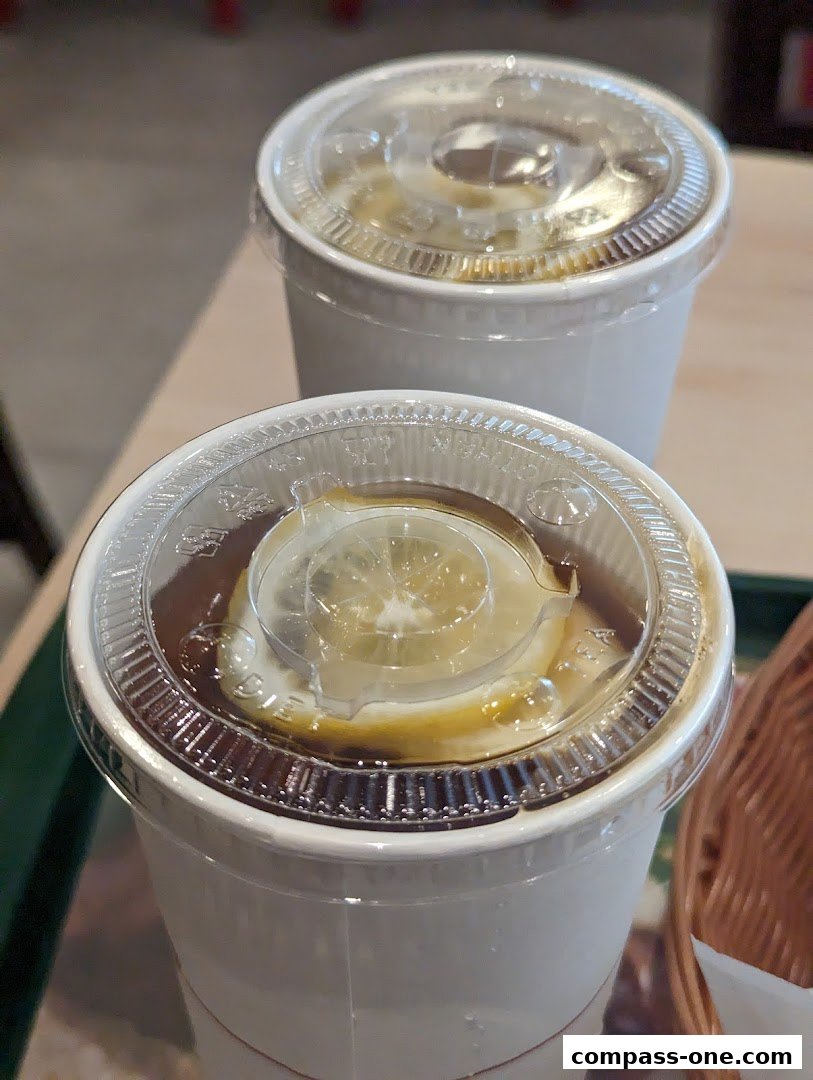 Two white cups with clear lids, one containing a drink with lemon slices.
