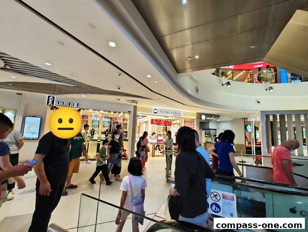 People walking in a mall with shops like Ho Bee Goldsmith and MoneyMax visible.