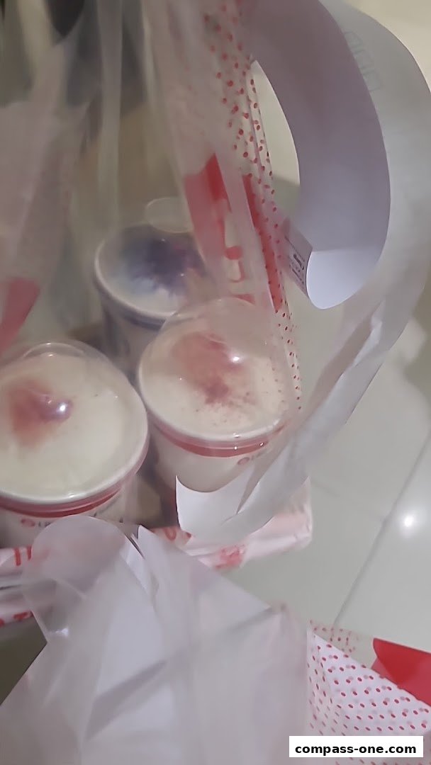 Three takeaway cups with drinks inside a white shopping bag with red polka dots.