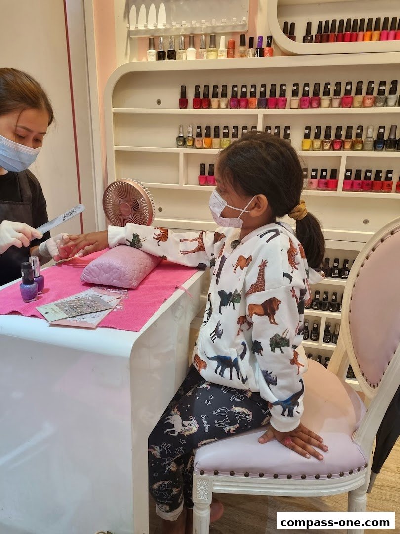 A nail technician files a young girl's nails at a salon with shelves of polish.