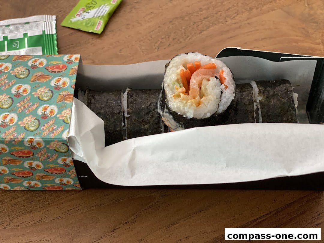 A box of Maki-San sushi rolls with sauce packets on a wooden surface.