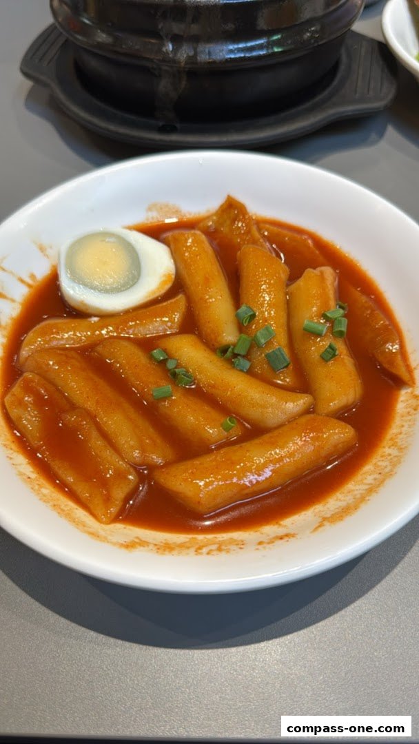 A bowl of Korean Tteokbokki with a boiled egg and chopped scallions.