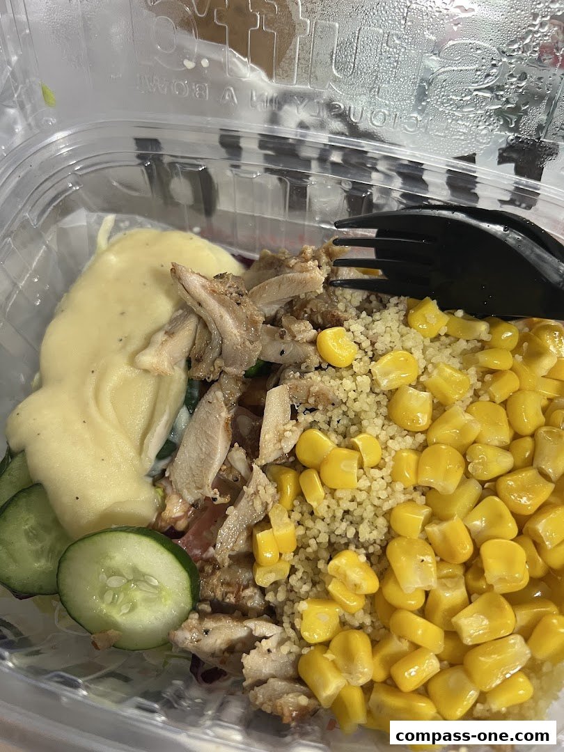A close-up of a salad bowl with chicken, couscous, corn, cucumber, and a creamy dressing.