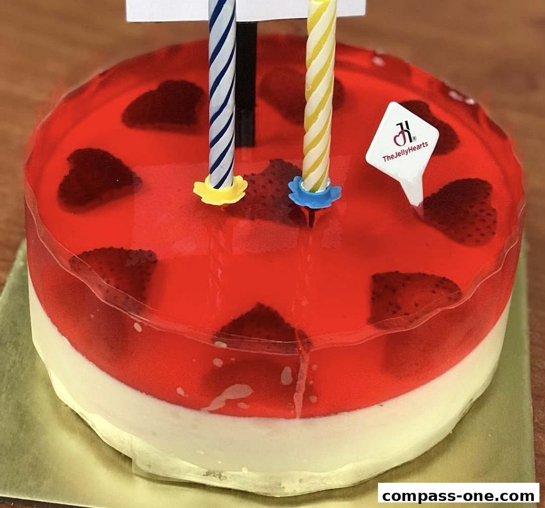 A close-up of a strawberry jelly cake with two birthday candles and the shop's logo.