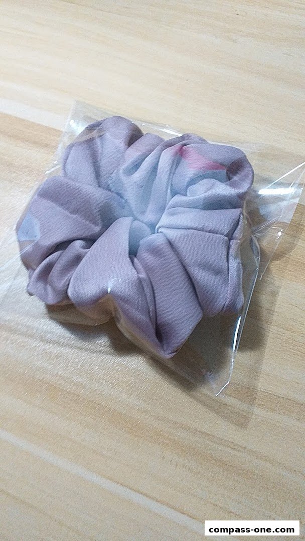 A close-up shot of a scrunchie with a pastel floral pattern, packaged in clear plastic.