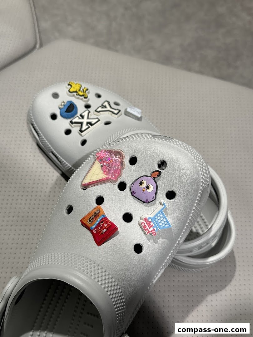 Two grey Crocs shoes adorned with various colorful Jibbitz charms.