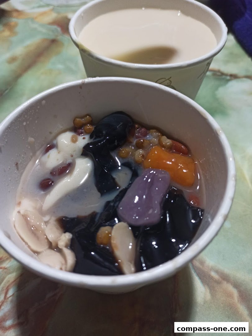 A close-up of two bowls of Taiwanese desserts, one with grass jelly and toppings, the other with a milky drink.