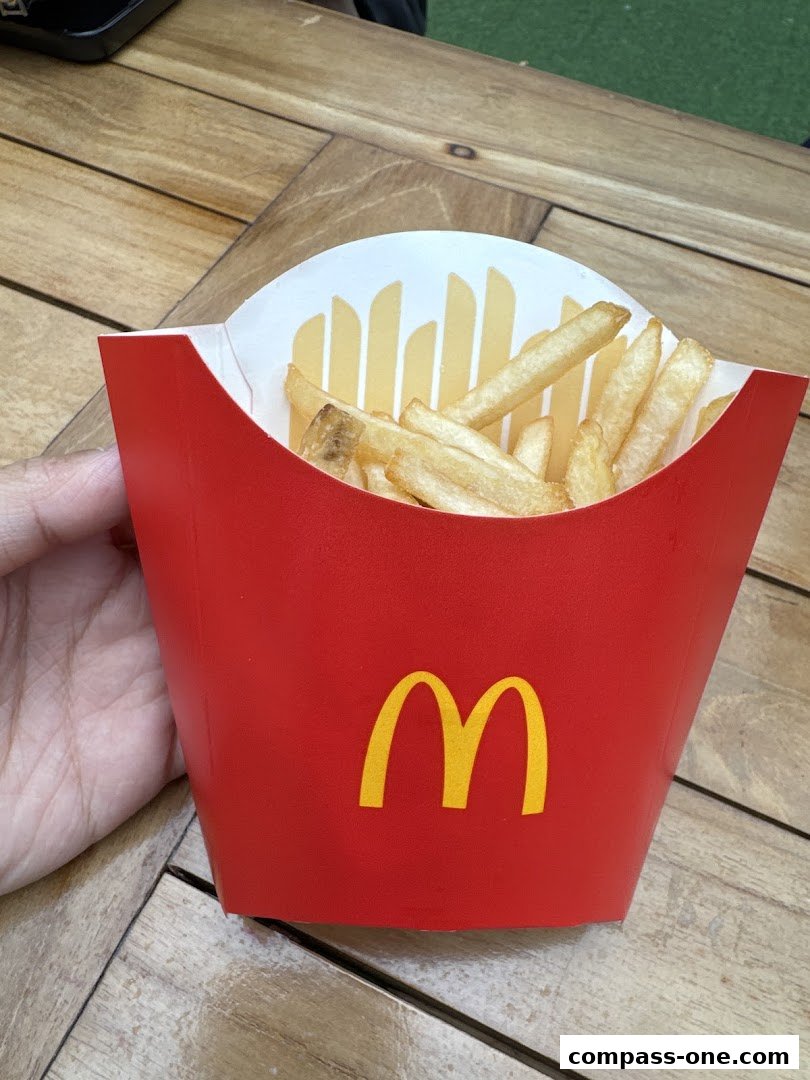 A hand holds a red carton of McDonald's french fries on a wooden table.