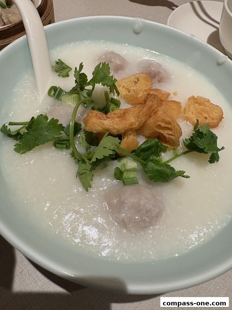 A close-up of a bowl of congee with meatballs, fried dough, and cilantro.