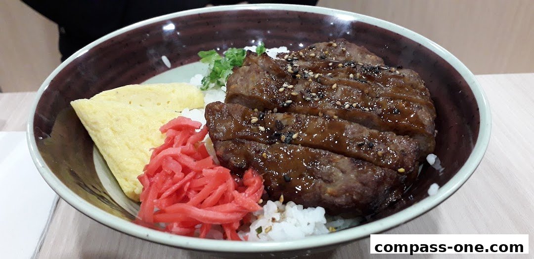 A close-up of a Japanese rice bowl with sliced teriyaki beef, tamagoyaki, and pickled ginger.