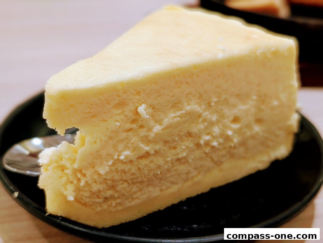 A slice of creamy cheesecake served on a black plate with a spoon.