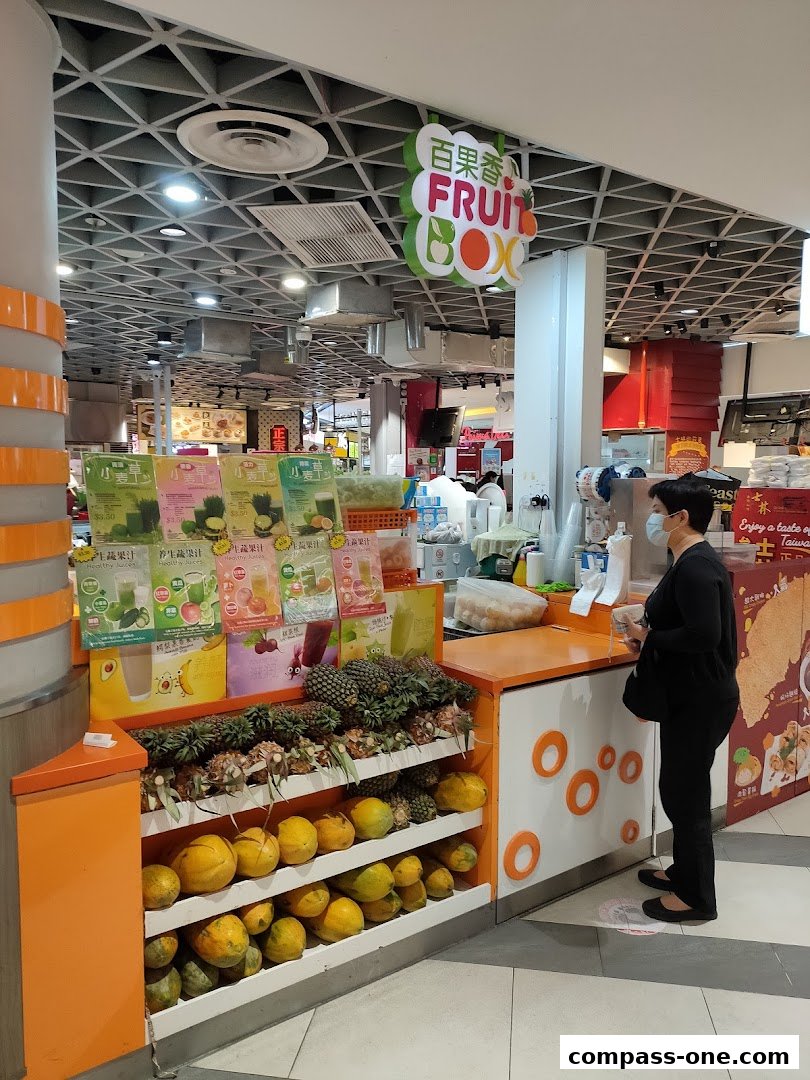 A fruit stall with a variety of fresh fruits and juices displayed, and a customer being served.