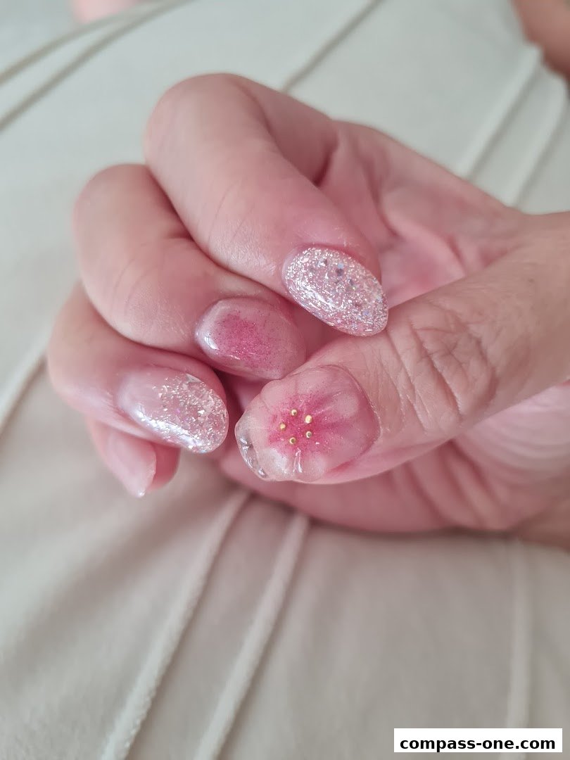 Close-up of a hand with beautifully decorated nails featuring glitter and floral designs.