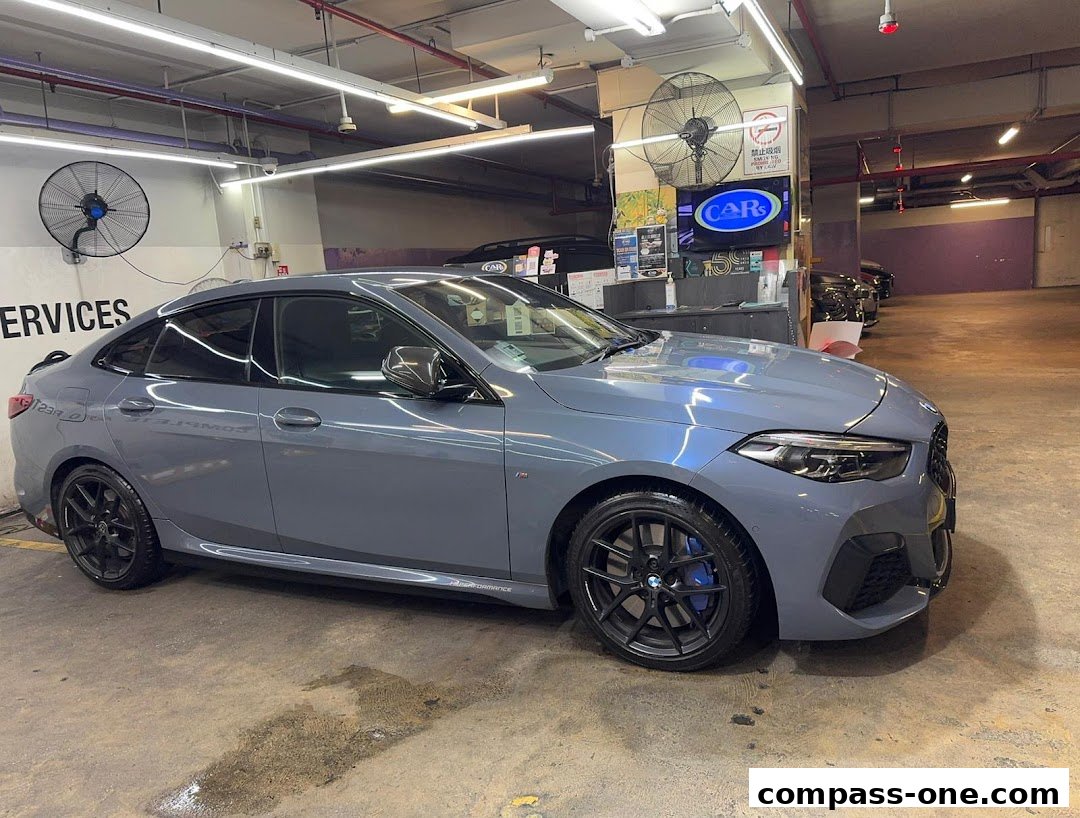A sleek grey BMW sedan is parked inside a well-lit garage with car detailing services visible.