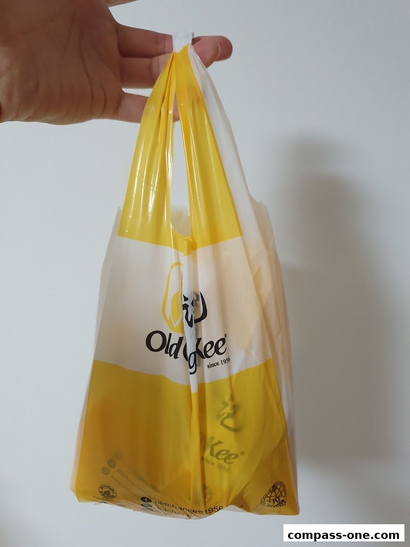 A hand holds a yellow and white plastic bag from Old Chang Kee.