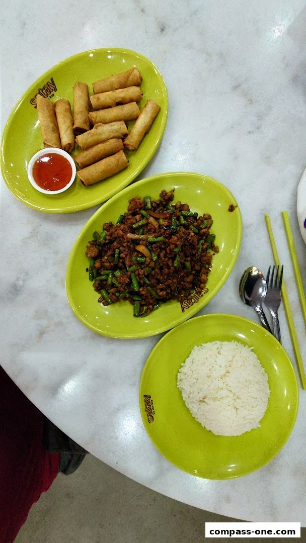 A table setting with Thai cuisine dishes including spring rolls, stir-fried meat with vegetables, and rice.