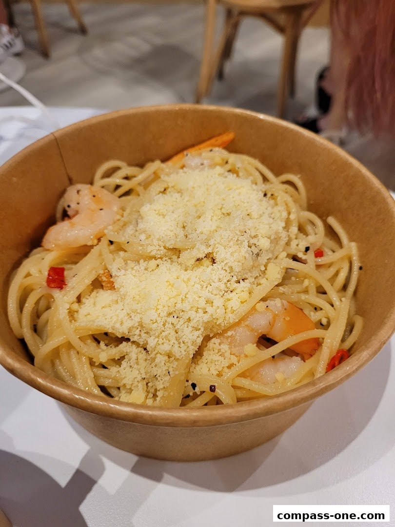 A close-up of a bowl of spaghetti with shrimp, garlic, chili, and grated cheese.
