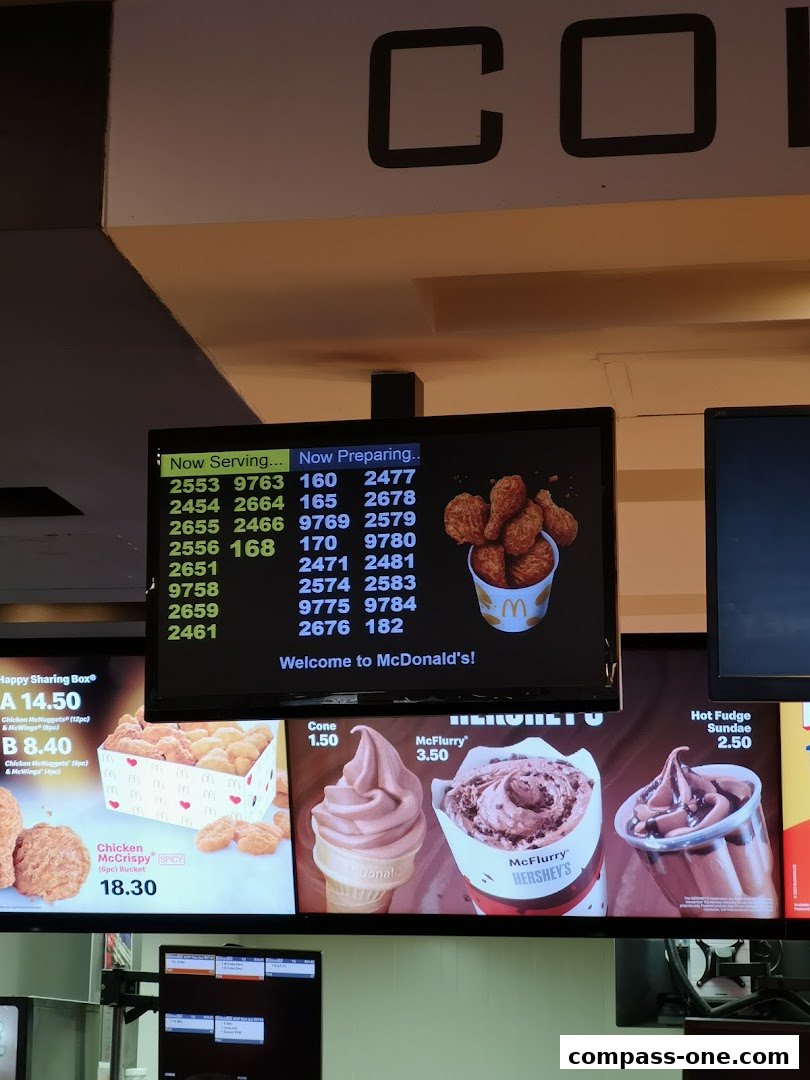Digital menu board displaying order numbers, food items, and prices at McDonald's.