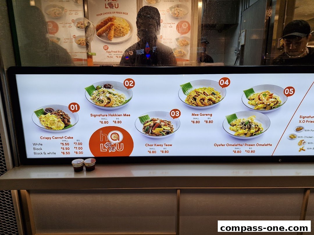 A digital menu board displaying various noodle and rice dishes with prices.