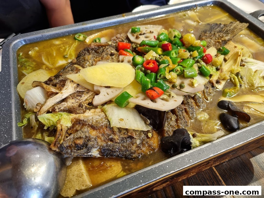 A close-up of a grilled fish dish with vegetables and spices in a metal tray.