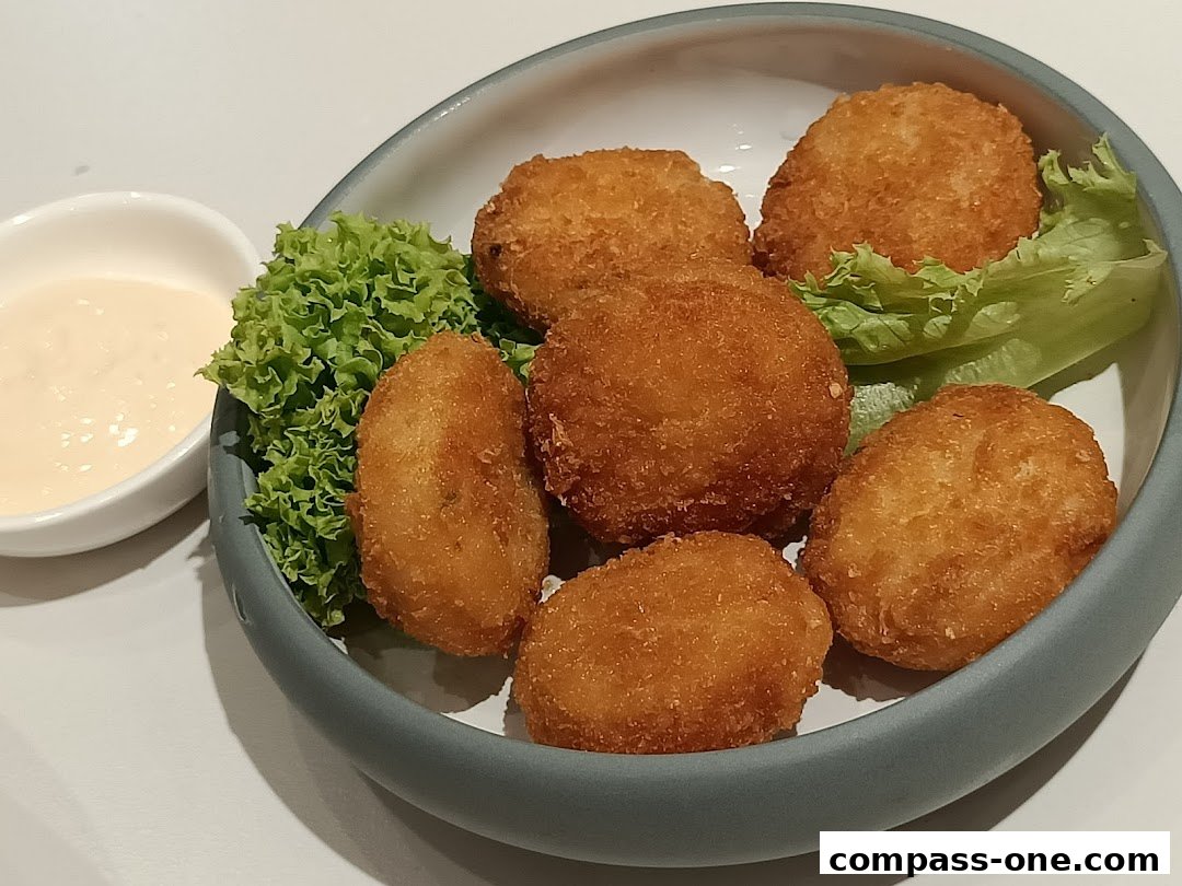 A bowl of golden-brown fried croquettes served with a side of creamy dipping sauce and lettuce.