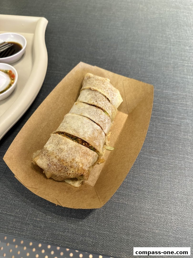 A freshly prepared popiah, sliced and served in a brown paper tray with dipping sauces.