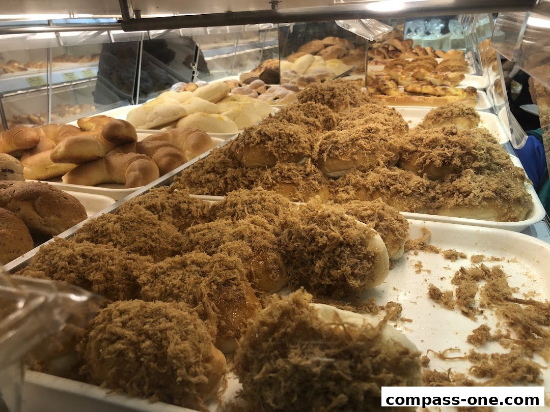 A display of freshly baked bread and pastries, including buns topped with shredded meat.