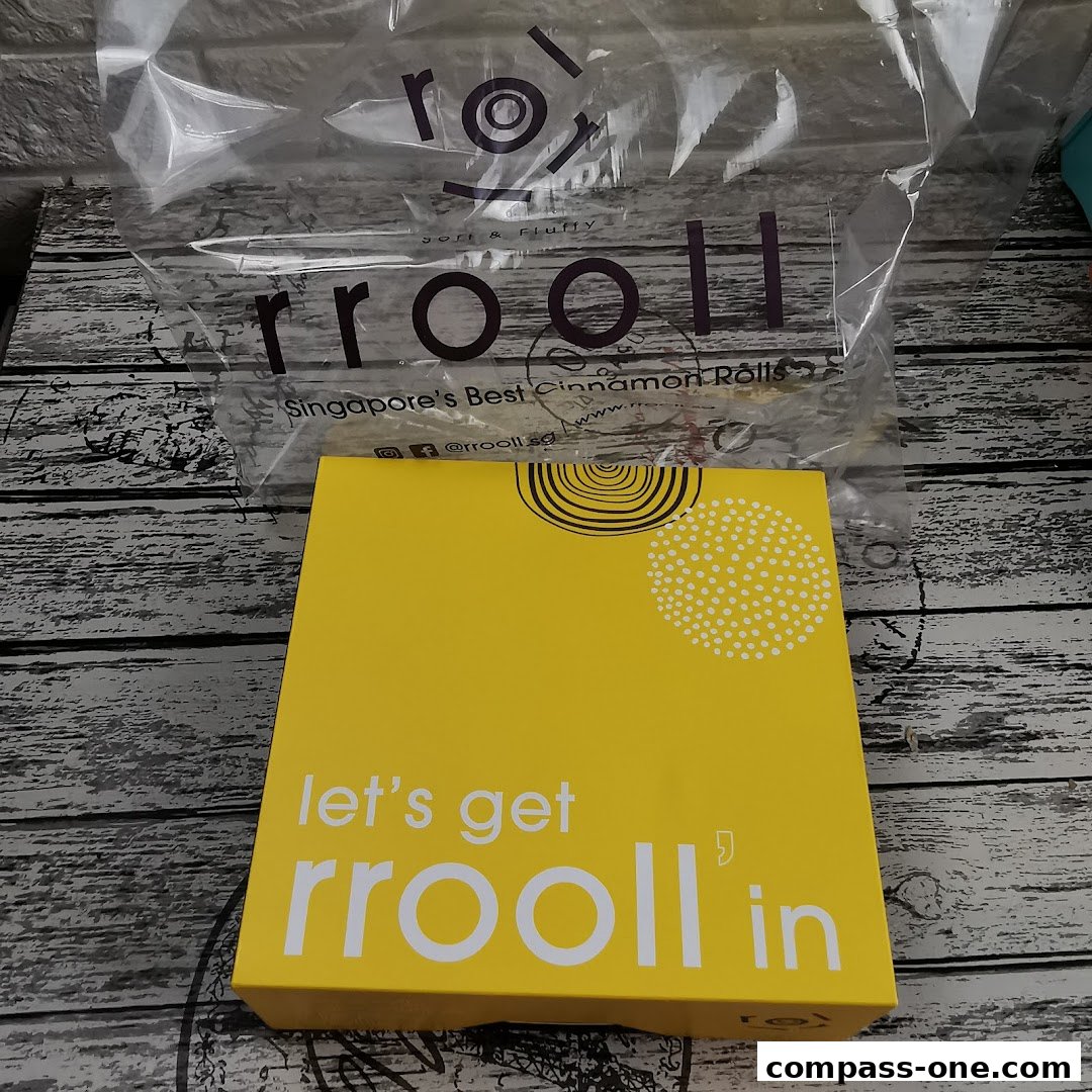A yellow box and a plastic bag with the rrooll logo and text about cinnamon rolls.