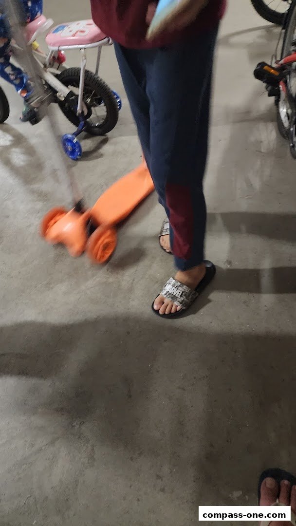 A person wearing Marvel slides stands near a child's scooter and bicycle.