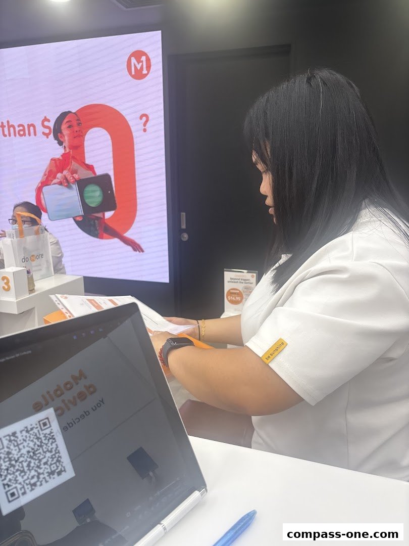 A shop assistant works at a counter with a digital display and a laptop.