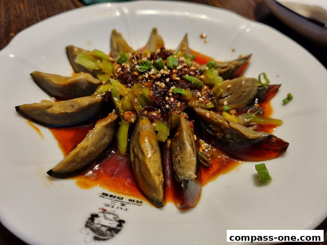 A plate of sliced preserved eggs with chili oil, scallions, and sesame seeds.