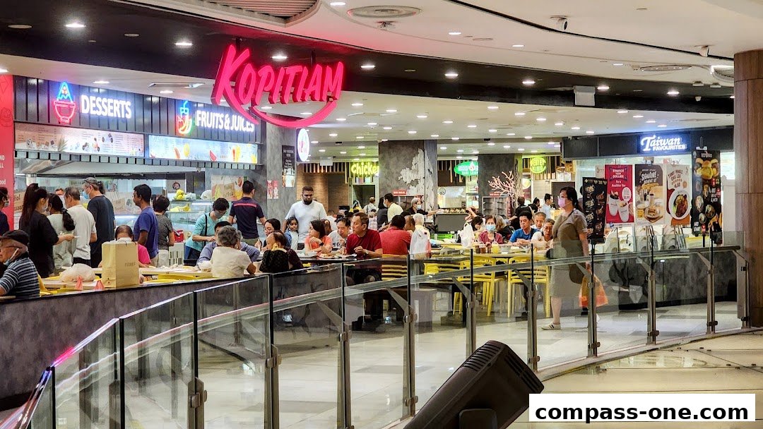 A busy food court with people dining at tables under the 'Kopitiam' sign.
