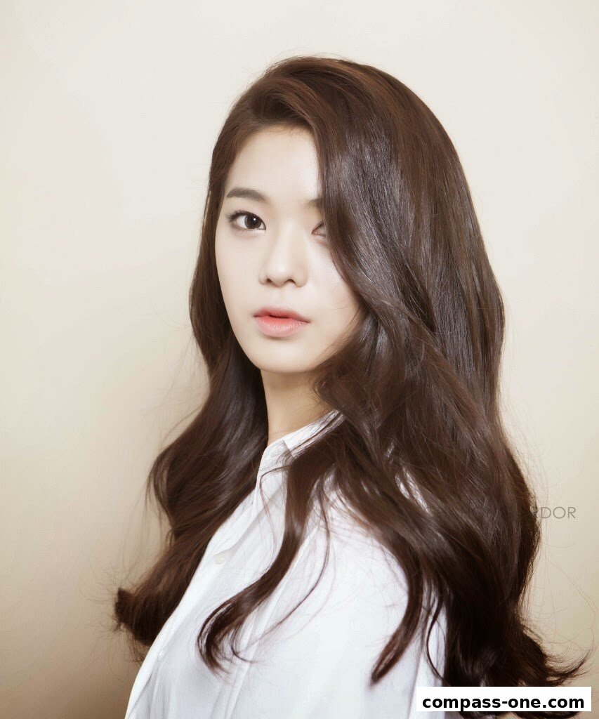 A young woman with long, wavy brown hair and a white shirt.
