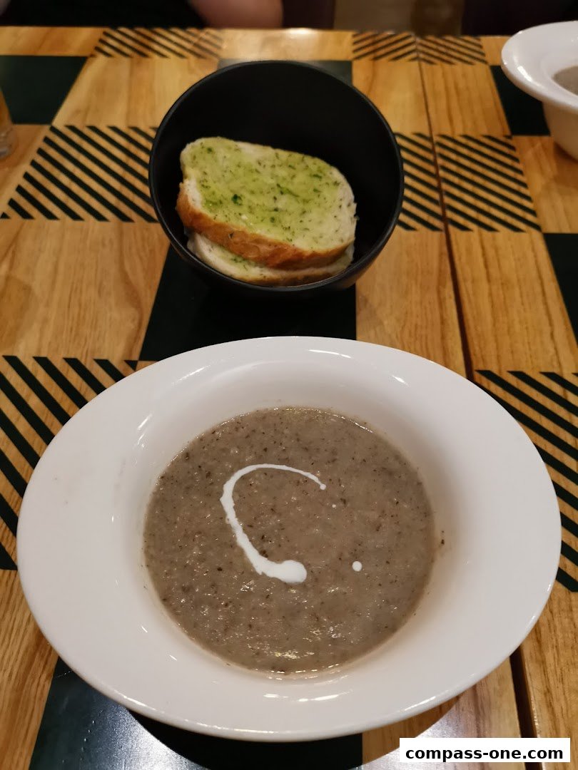 A bowl of mushroom soup with a swirl of cream and garlic bread slices on a wooden table.