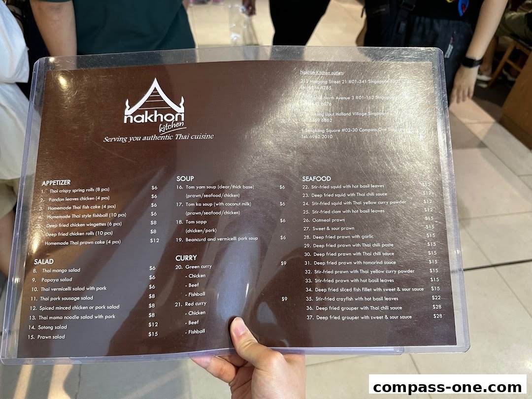 A person holds a menu from Nakhon Kitchen, showcasing authentic Thai cuisine with various dishes and prices.