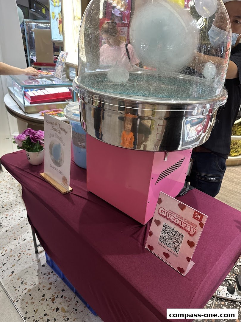 A cotton candy machine is set up with a giveaway sign and a display of jewelry in the background.
