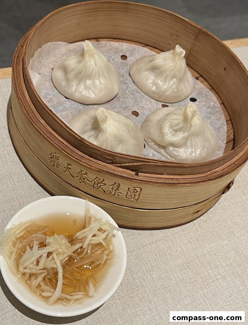 A bamboo steamer filled with four delicious soup dumplings and a side of pickled ginger.