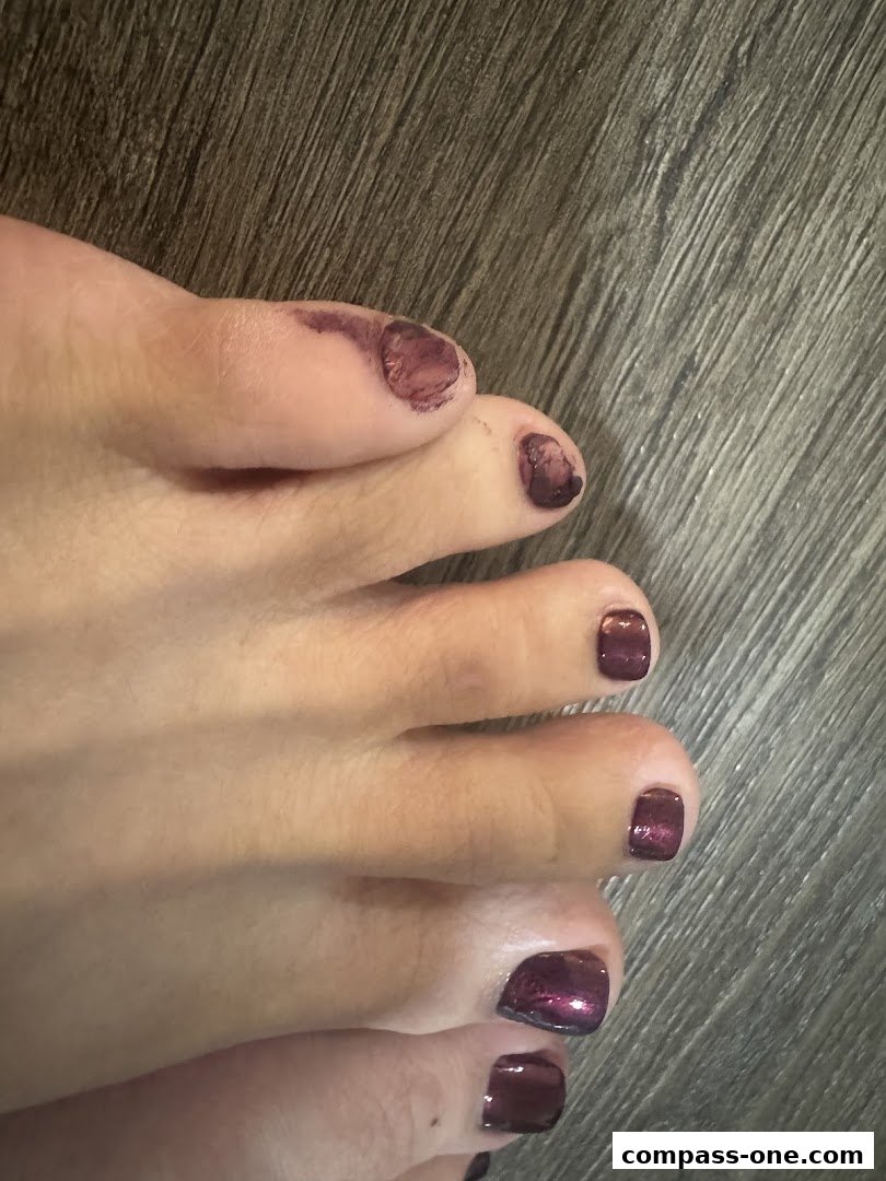 Close-up of toes with dark purple, shimmery nail polish, some smudging visible.