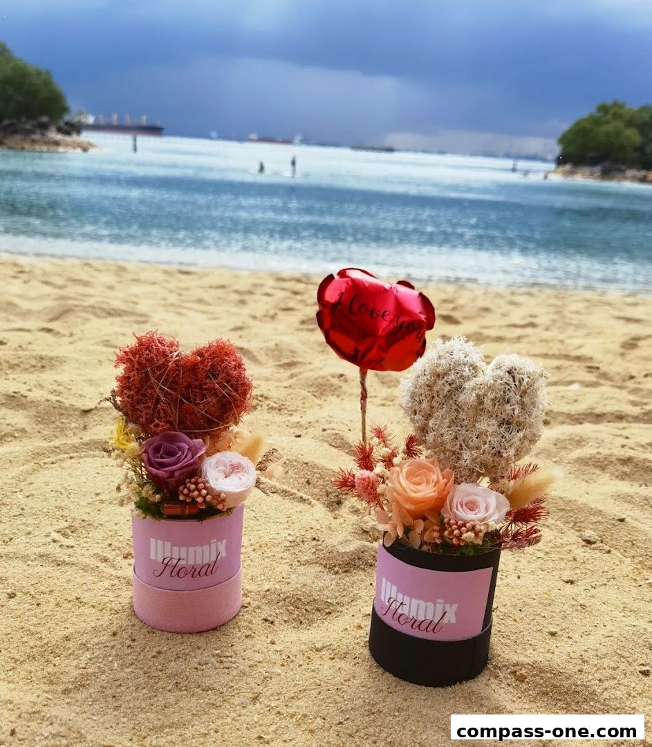 Two floral arrangements with heart shapes and a red balloon on a sandy beach.
