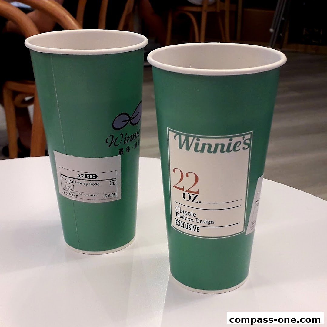 Two green paper cups from Winnie's, one with a label for Floral Honey Rose.