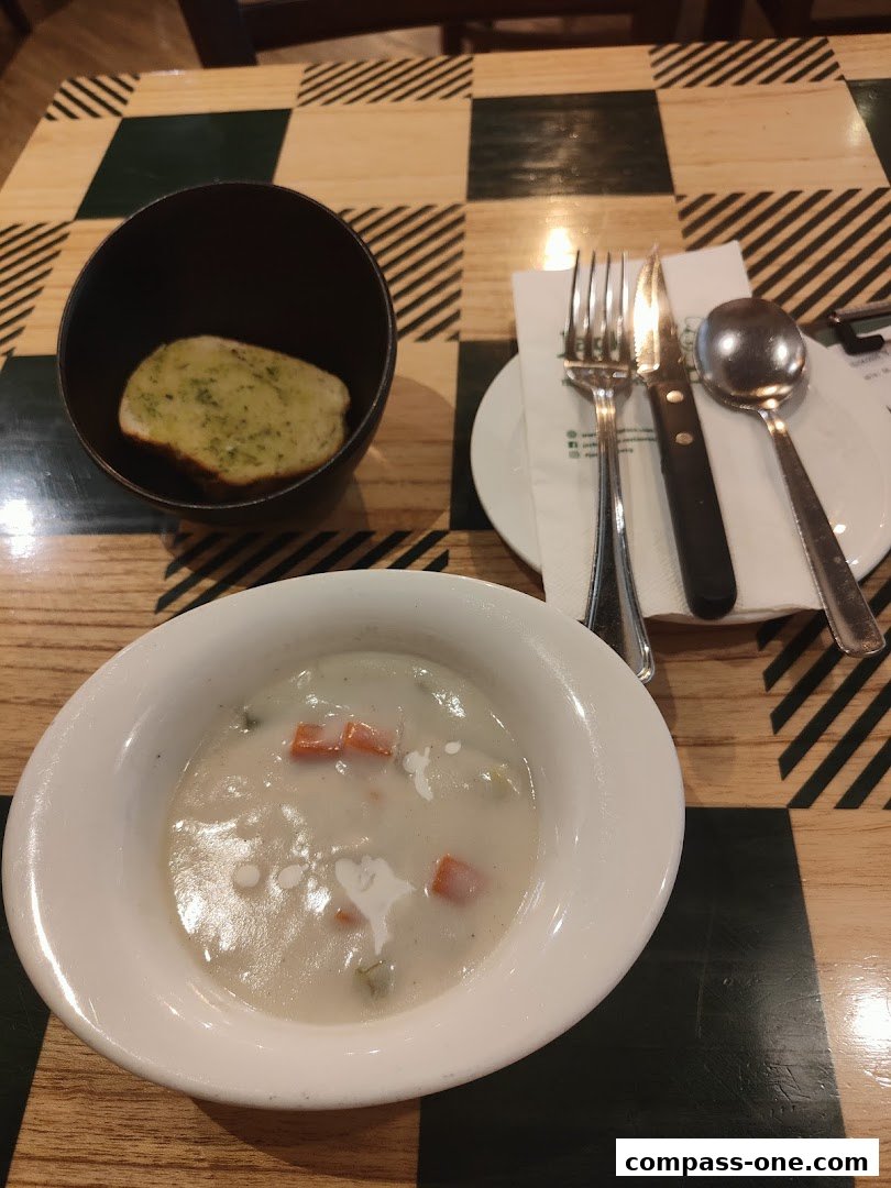 A bowl of creamy soup with vegetables and a slice of garlic bread on a checkered table.