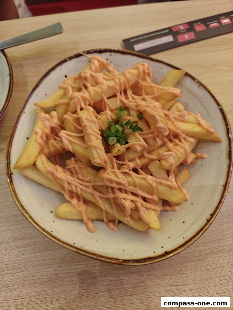 A bowl of crispy fries topped with a creamy pink sauce and garnished with chopped green onions.