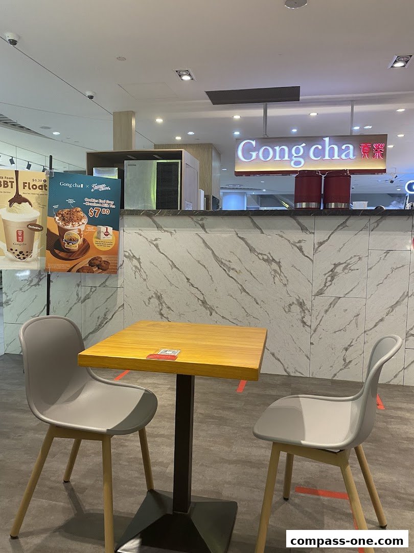 A table and chairs in front of the Gong Cha counter with promotional posters.