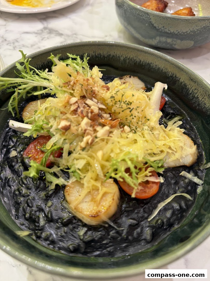 A close-up of a dark, creamy dish topped with scallops, salad, and nuts.