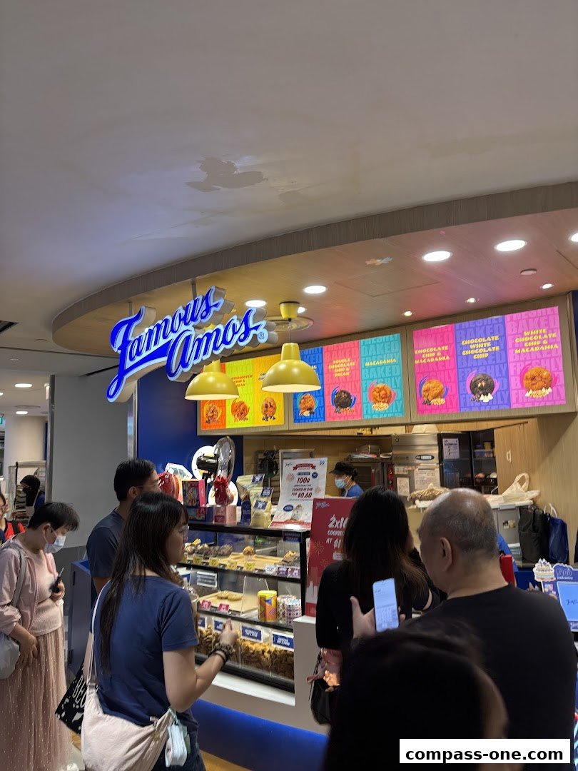 A Famous Amos cookie shop with customers queuing and cookies displayed in a display case.